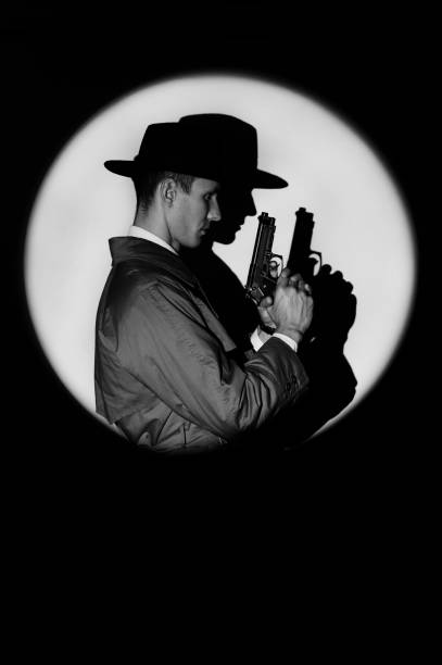 une silhouette sombre d’un détective masculin vêtu d’un manteau et d’un chapeau avec un pistolet à la main dans le style noir. un portrait dramatique dans le style des films policiers des années 1950. la silhouette d’un espion dans un cercle de - police crime gun gang member photos et images de collection