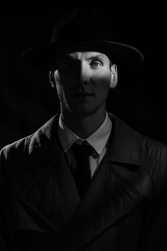 A dark silhouette of a male detective in a coat and hat with a noir style. A dramatic noir portrait in the style of detective films of the 1950s