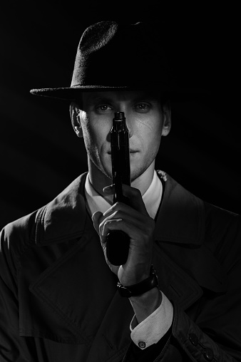A dark silhouette of a male detective in a coat and hat with a gun at his face in the Noir style. A dramatic noir portrait in the style of detectives of the 1950s