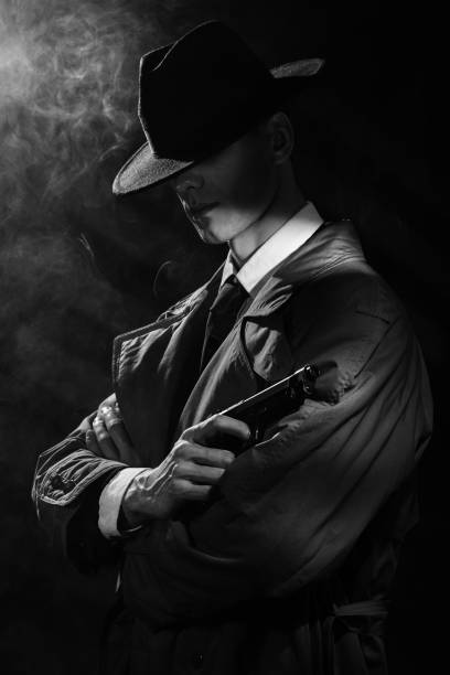 une silhouette sombre d’un homme en imperméable et chapeau avec un pistolet à la main dans le style du crime noir. un portrait noir dramatique dans le style des détectives des années 1950. - police crime gun gang member photos et images de collection