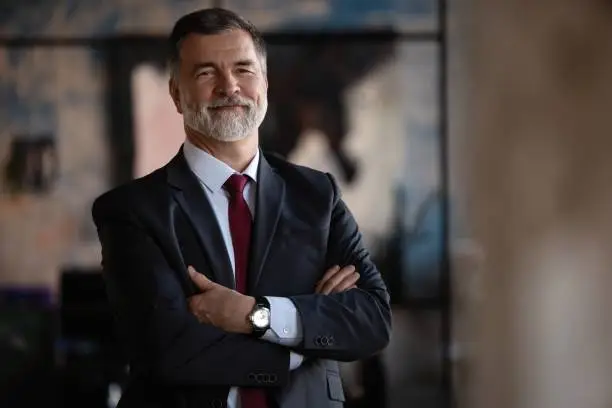 Photo of Confident mature business man with arms crossed looking at camera, smiling standing in modern office