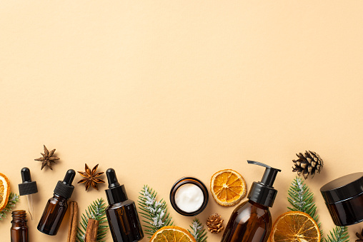 Organic cosmetics concept. Top view photo of cosmetic bottles fir branches in frost pine cones cinnamon sticks and dried citrus slices on isolated beige background with copyspace