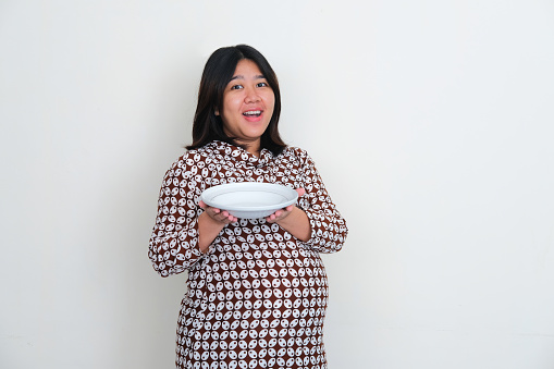 Pregnant Asian women showing empty dinner plate with happy expression