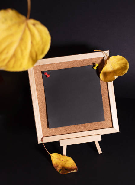 istock Yellow fall leaves and small decorative wooden easel with empty black sheet on black background. 1438147728