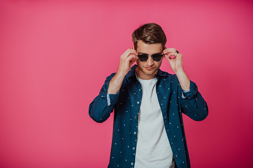A portrait of a young man wearing a blue shirt and posing in front of a pink background. High quality photo