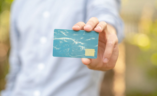 Man holding a simple blank empty plastic credit card or gift card in his hand, presenting it to the camera, copy space, shallow dof, modern design. Giving, handing, showing a club card concept