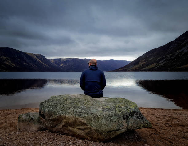 homem sentado contemplando em um lago na escócia - self reflection - fotografias e filmes do acervo