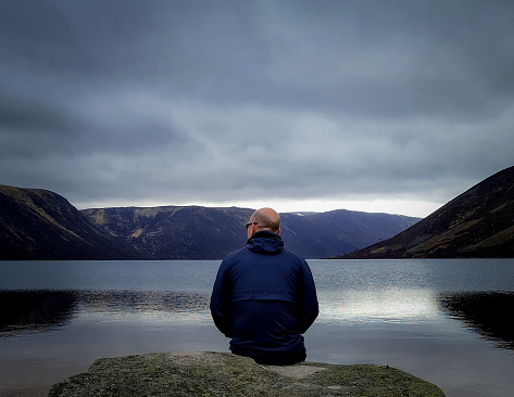 Man sits by himself in quiet contemplation on a dark day at loch Muick near Ballater