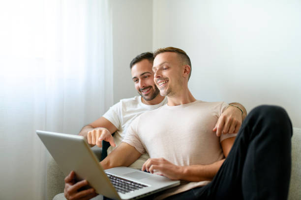 istock Happy young two man couple using laptop computer while sitting on a couch at home 1438150039