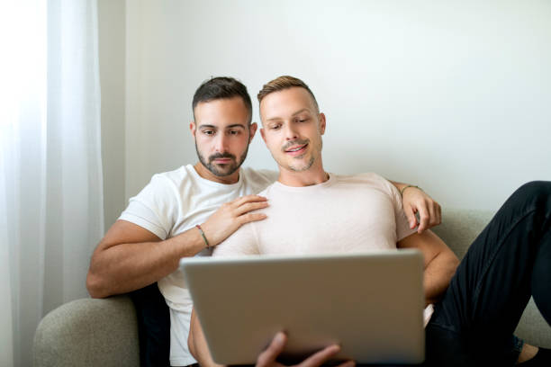 istock Happy young two man couple using laptop computer while sitting on a couch at home 1438150041