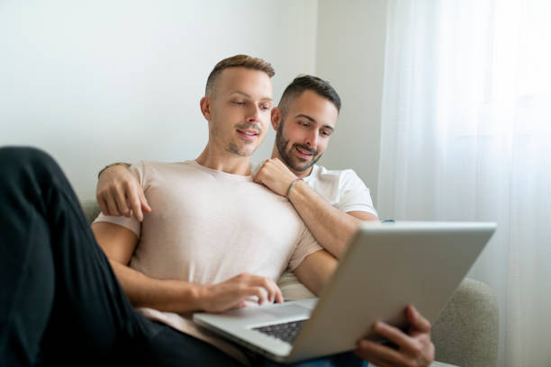 istock Happy young two man couple using laptop computer while sitting on a couch at home 1438150043