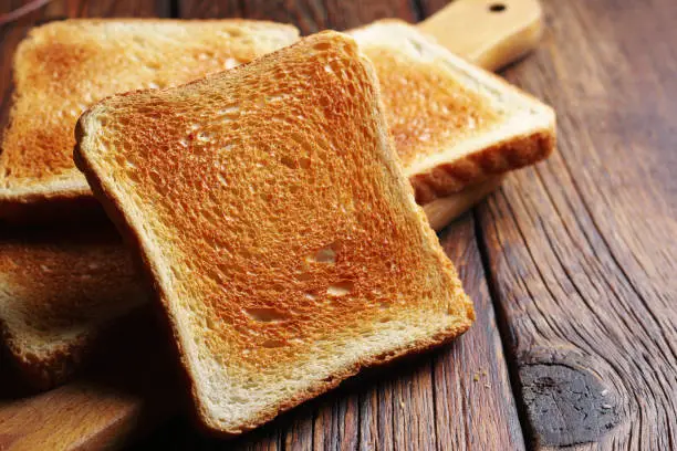 Slices of toasted bread on kitchen board on wooden table close up