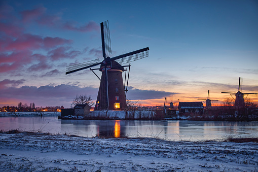 Several windmills in winter at the Kinderdijk, Holland. The water is frozen and all the land is covered with snow. The sun is gone.