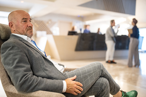 A senior businessman sitting in an armchair in a hotel's lobby before a business conference