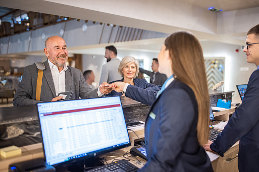 A senior businessman handing his credit card to a hotel reception worker in a luxury hotel