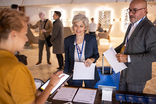 Two mature business people registering for a conference event in a luxury hotel lobby