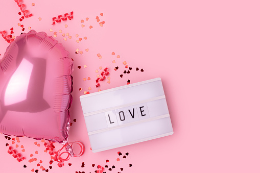 Word Love. Lightbox, confetti and inflatable foil balloon in a heart shape on a pink background. Place for text.