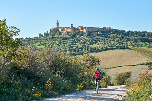 nice senior woman riding her electric mountain bike in the Ghianti area beow the skyline of the medieval city of Pienza , Tuscany , Italy