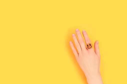 Female hand with smiley ring made of beads on a yellow background. Place for text.