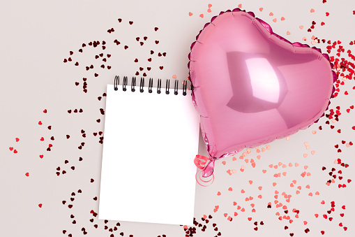 Blank notepad mockup, confetti and pink inflatable foil balloon on a gray background. Festive concept.