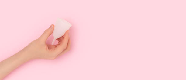 istock Banner with female hand hold white menstrual cup on a pink background. 1438159587