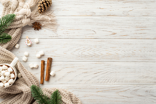 Winter concept. Top view photo of pine cone spruce branches mug of cocoa scattered marshmallow knitted plaid decorative clip anise and cinnamon sticks on white wooden desk background with copyspace