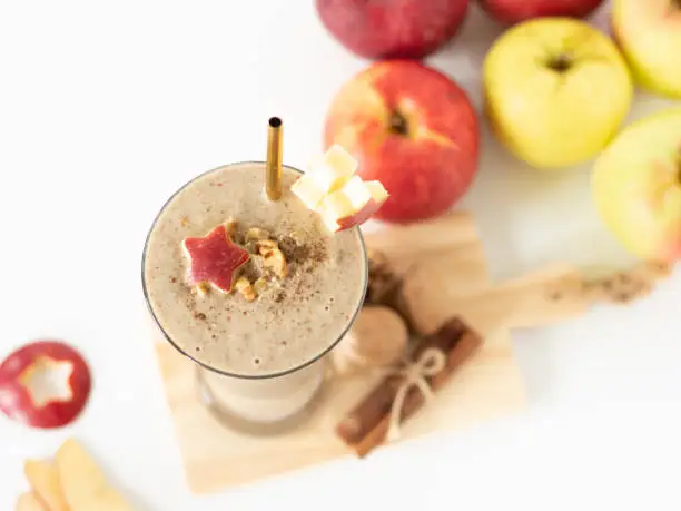 Apple smoothie with cinnamon, oats, and walnuts on white background with red and green apples. Top table view. A close-up. Plant-based autumn breakfast shake.