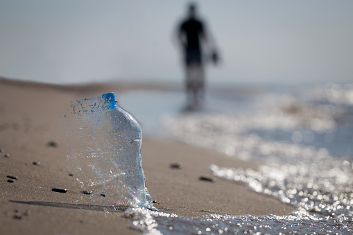 Close-up, selective focus, PET plastic bottle. Garbage left on a sandy beach. Creartive concept, disintegration effect.