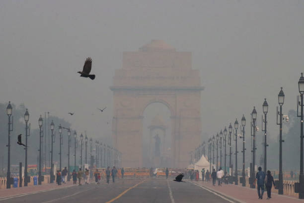 Image of All India War Memorial / New Delhi India Gate surrounded by hazy sky pollution, crowds of tourists on Kartavya Path (Rajpath), polluted foggy misty sky stock photo