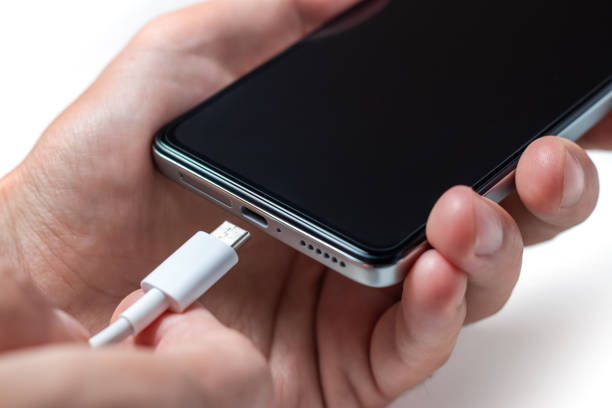 istock Charging a smartphone via a USB cable and a power supply. A black smartphone hanging with a usb charging cable. 1438169369