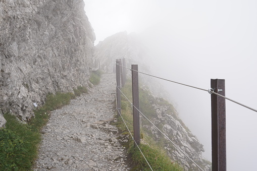 Tourist path in the mount Pilatus in Switzerland Alps folded in mist. Trail is from right side protected by metal post and steel wire and on the left side is steep rock.
