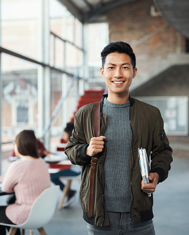 Student, smile and happy man from China in a study, exam and education learning in a study hall. Portrait of a university, college, and scholarship Asian person with happiness with test books