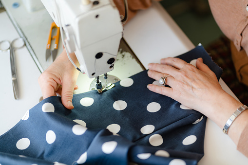 Close up of sewing machine and seamstress's hands sewing clothes