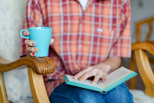 Close up of female hands with book and hot drink. Female reading book