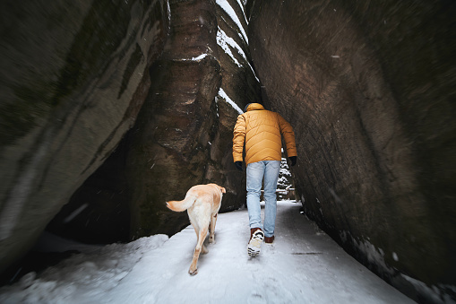 Man with dog during winter hike. Pet owner walking on snowy footpath with his labrador retriever in middle of rocks.
