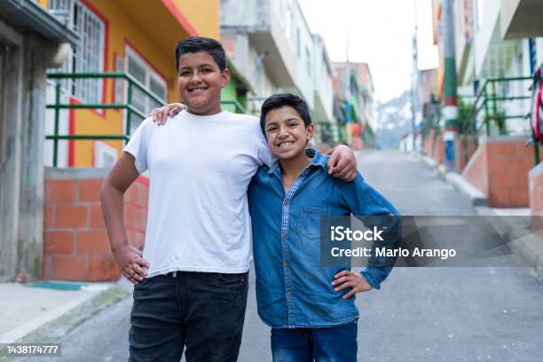 Latino Brothers Are On The Street Of The Neighborhood Where They Live Looking Towards The Camera That Portrays Them Stock Photo - Download Image Now