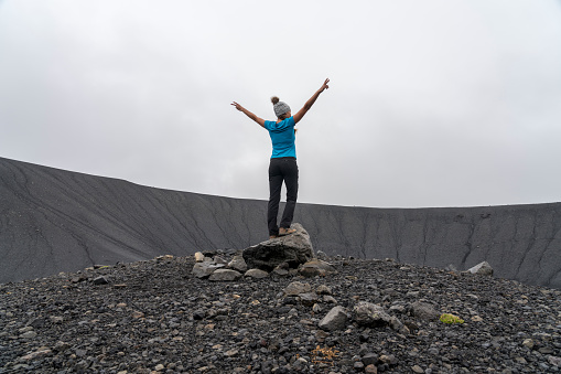 One women at the bottom of the Hverfjall volcanic crater with arms raised.  Hverfjall, is one of the best preserved circular volcanic craters in the world and it is possible to walk around and inside it.