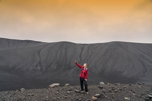 One women at the bottom of the Hverfjall volcanic crater making selfie.  Hverfjall, is one of the best preserved circular volcanic craters in the world and it is possible to walk around and inside it.