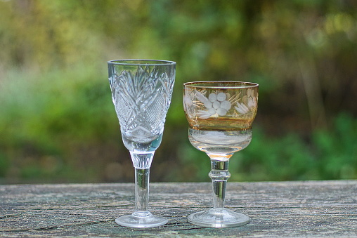 a two of white and brown glass crystal goblets on a gray wooden table outdoors on a green background