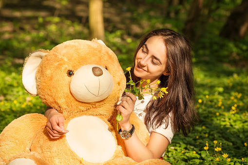 girl with teddy bear sitting on grass in forest