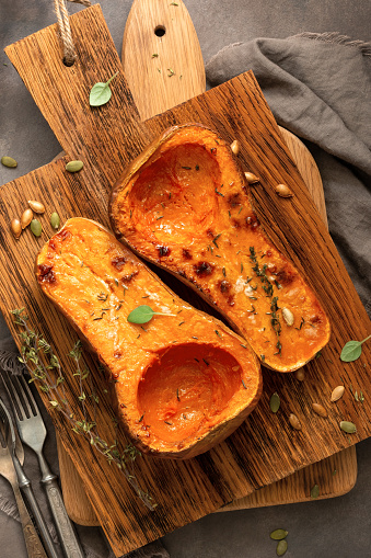 Baked pumpkin halves with herbs on a wooden cutting board. Baked butternut squash. Thanksgiving and Halloween concept. Top view, flat lay.