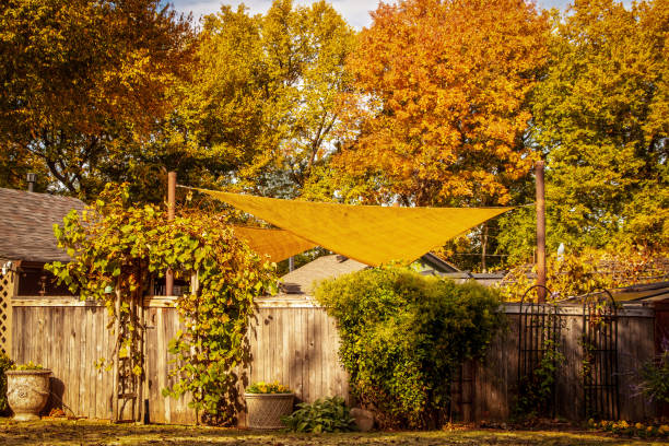 October golden yellow shade sail over enclosed garden or party area with arched vine covered entry with potted flowers and autumn leaves background stock photo