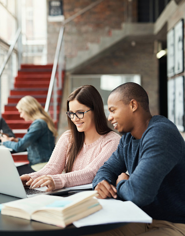 Student, working and study friends together with a computer using technology for university research. Scholarship, education and college library test learning of a black man and woman with a laptop