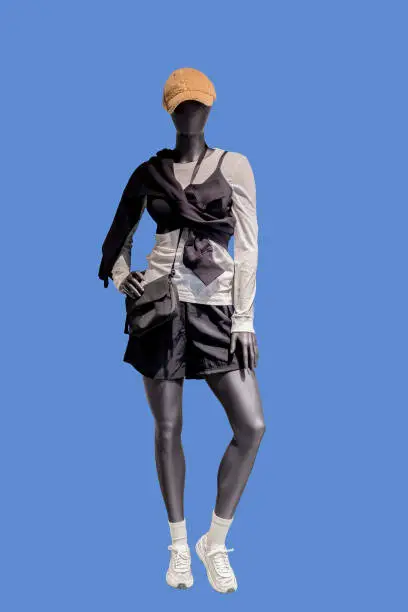 Full length image of a female display mannequin wearing white sports shirt and black shorts isolated on blue background