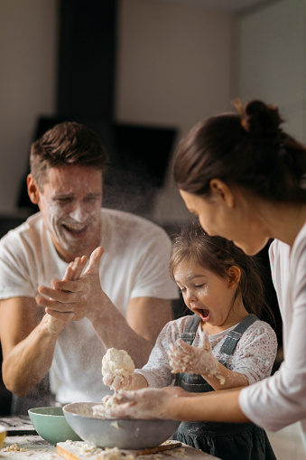 family having fun during pastry preparing, flour flying all around the modern kitchen