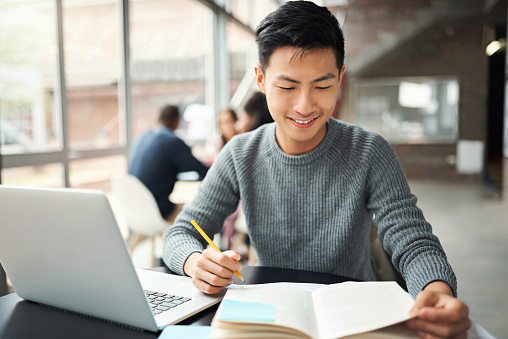 Asian man, laptop and notebook in education, learning or study on college, university or Japanese school campus. Smile, happy and graduate for law student with technology and legal scholarship books