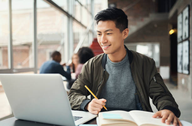 studente universitario, uomo asiatico e studio su laptop al campus, test di ricerca e istruzione, libri d'esame e progetto di corso. felice studente universitario giapponese, conoscenza e apprendimento della tecnologia online - studing foto e immagini stock