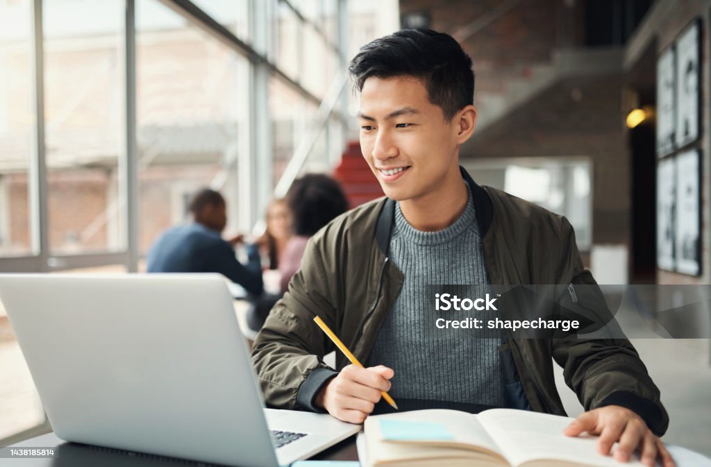 College student, asian man and studying on laptop at campus, research and education test, exam books and course project. Happy Japanese university student, knowledge and learning online technology Student Stock Photo