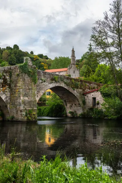 Medieval Roman bridge reflected on the water of the river Arnoia in the Galician village of Allariz on a rainy morning.