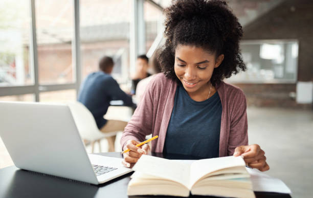 istock Laptop, book and black woman student studying on college campus table for language learning, education or online research. Scholarship, university and girl with literature for English project or exam 1438186574